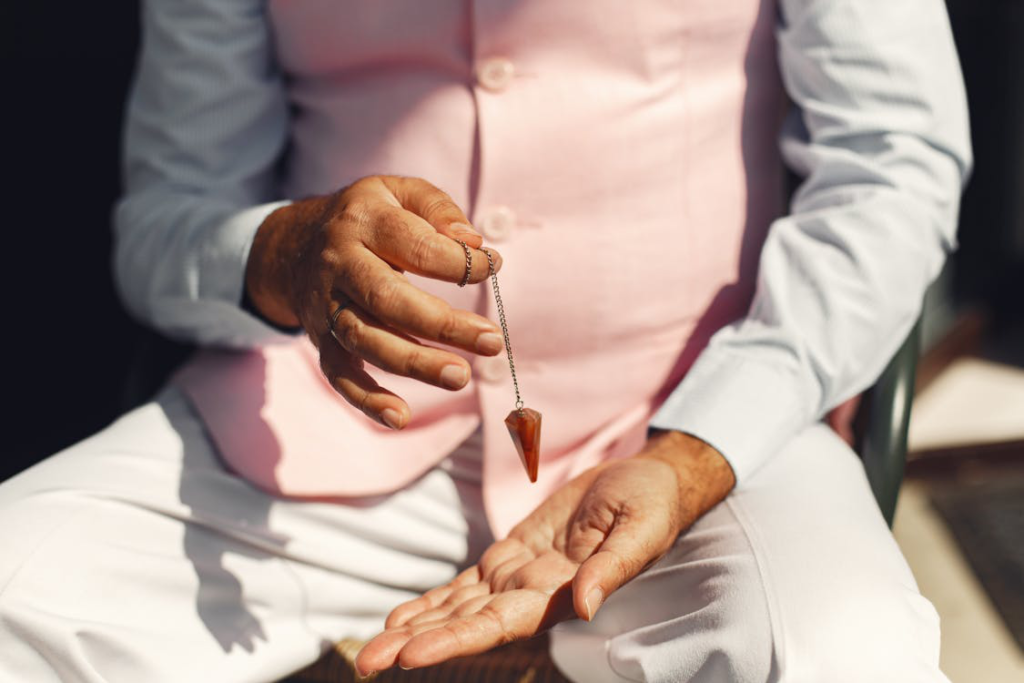 A person wearing a pink waistcoat holding a necklace with a gemstone